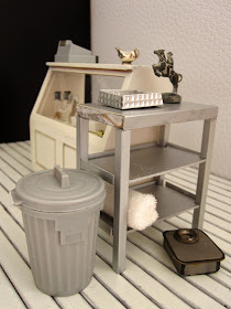 Corner of a modern dolls' house miniature interiors shop, with a range of items in grey, silver and white on display.