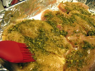 Basting chicken breasts with pesto sauce.