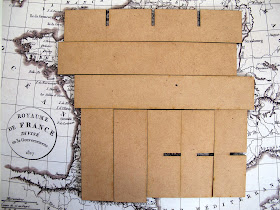 Components of a  modern dolls' house miniature laser-cut 'pidgeon' hole kit laid out on a piece of scrapbooking paper showing a vintage map of France.