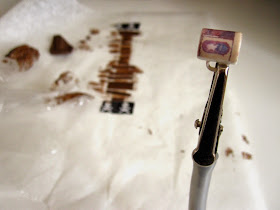 Modern dolls' house miniature mug with decal attached, in front of stained components of a  tea bag box laid out to dry.