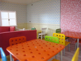 Interior of the ground floor of a half-built Lundby dolls' house, with tables and chairs.