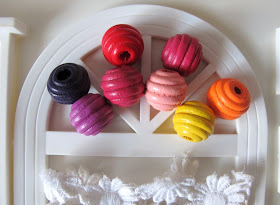 Eight coloured wooden beads, arranged in the fanlight of a dolls' house miniature fanlight.