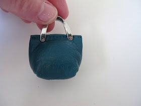 Hand holding up a dolls' house miniature leather handbag with metal straps.