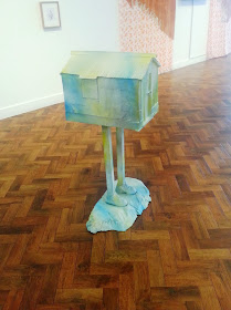 Ronnie van Hout's 'Cold shoulder to cry on' sculpture of a house on legs in a gallery.