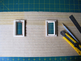 Wall of a dolls' house miniature kit, with window holes cut and windows installed.