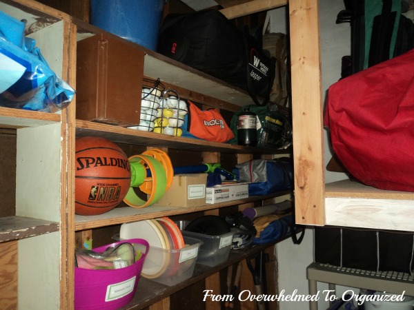 From Overwhelmed to Organized. Wooden shelves in garage organized with plastic bins, balls and sports gear.