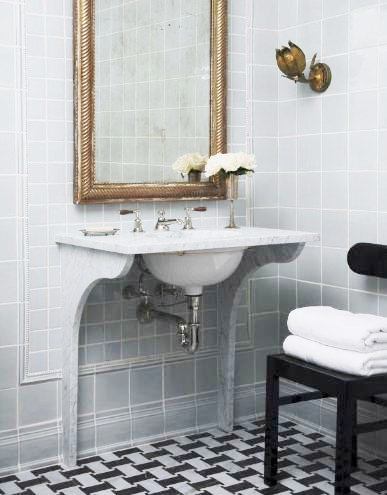 Bathroom with black and white marble mosaic floor and grey tiled walls, a wall mounted sink with an traditional antique mirror in a gold frame