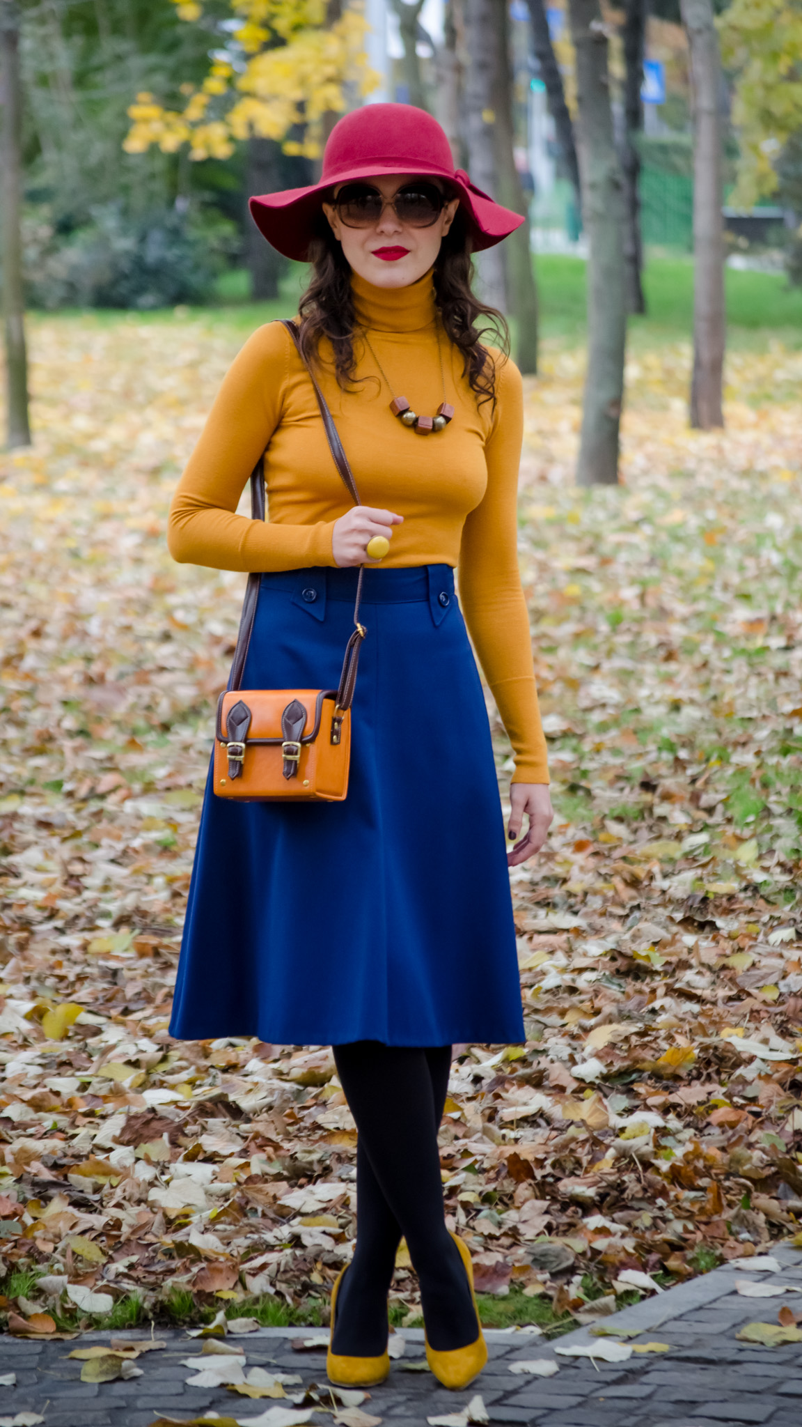 blue skirt mustard turtleneck sweater burgundy floppy hat brown jacket box satchel mustard heels autumn fall scenery leaves