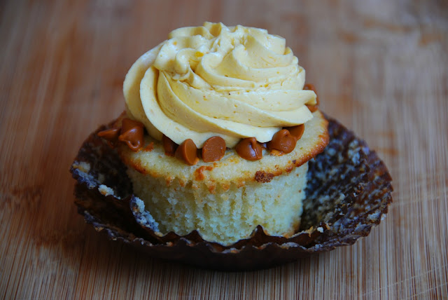 close up of unwrapped cupcake in brown wrapper with swirl of white icing on top