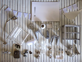 Selection of grey and white modern dolls' house miniatures arranged on  white-painted wood panelling. 