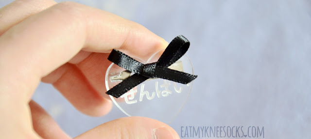 Milkstud Review: Heart Pins Close-up of the clear heart pin from Milkstud with a black ribbon and white engraved Japanese hiragana characters that say "senpai."