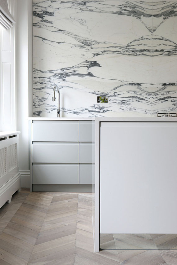 Minimalist kitchen with marble splashback and chevron oak floor