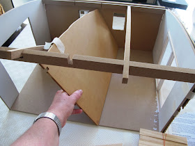 Close up of the Inside of a half-built dolls' house shed,with a hand holding a central wall at an angle because it doesn't fit where it should go.