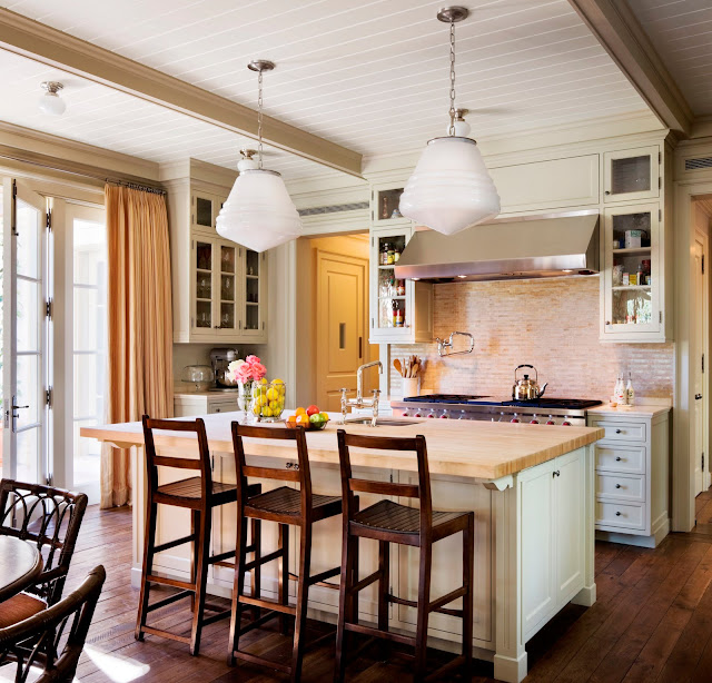 Kitchen from Kitchens and Baths by Michael S. Smith with two pendant lights, an island with wood counter top and white cabinets, stainless appliances, a brick backsplash, french doors and wood floors