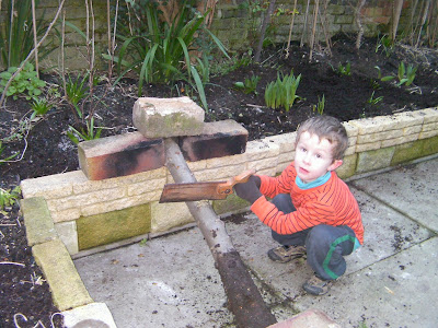 sawing an apple log up against brick raised flowerbed