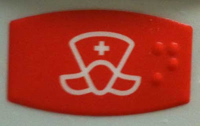 red button with white outline art in an odd shape with a small white cross in the center