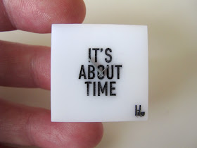 Hand holding a modern dolls' house miniature square perspex clock.