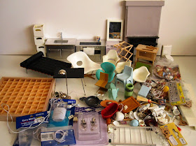 A large selection of modern miniature furniture and accessories, laid out on a  white workbench.