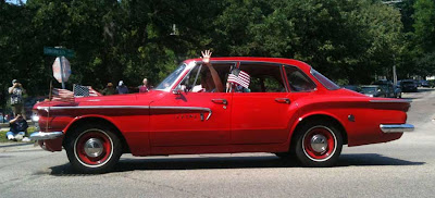 Red Dodge Lancer with a small American flag waving out the window