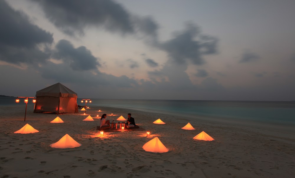 Photo of the young couple dining on the beach with candles 