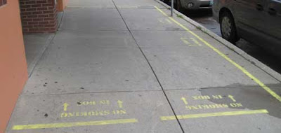 Sidewalk with yellow markings and stenciled lettering, making a box