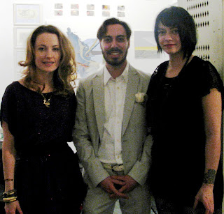 twom women in dark dresses and a man in a light grey suit pose for a photo