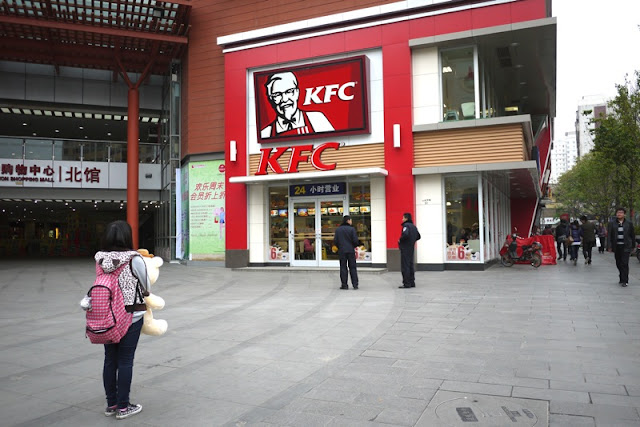 girl hold stuffed bear appearing to look at a KFC