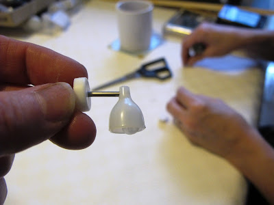 Woman holding a modern miniature wall lamp in front of table with a second woman working with wire in the background.