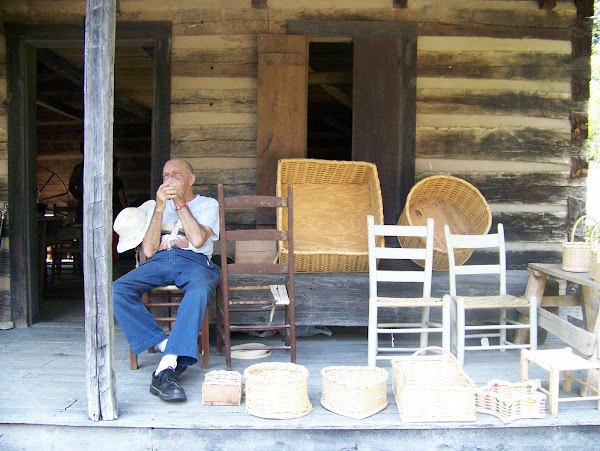 Willis Plott playing his jaw's harp beside the baskets he made and chairs he caned