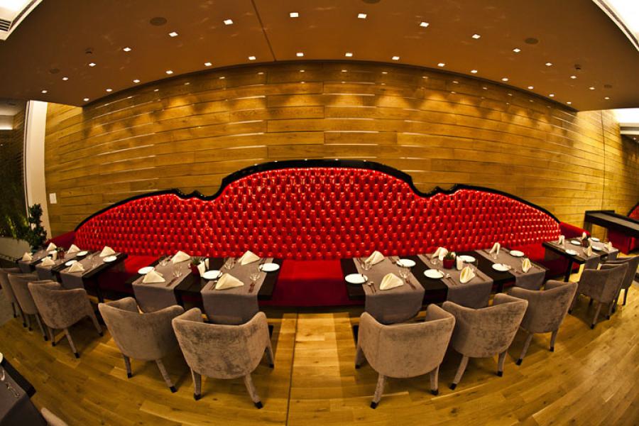 Picture of many square dining tables lined up by the huge long sofa with red leather on the wooden wall