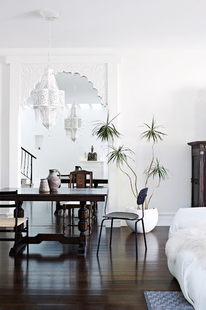 Dining room with white washed walls, carved white mirror Moroccan lamp with matching pendant light, dark wood floors and Middle Eastern inspired table and chair