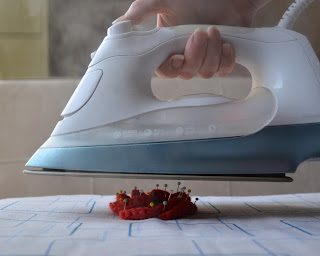 An iron steaming over an ironing board upon which is pinned a crocheted flower.