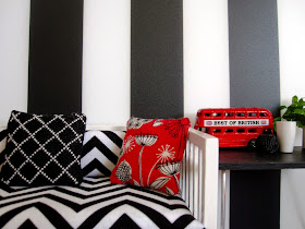 Modern miniature black white and red scene of a day bed with cushions next to a table displaying a model London bus and vases.