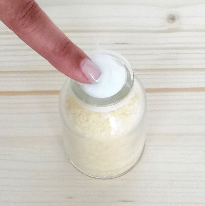 Una mano presionando algodón en un frasco de cristal con sal teñida