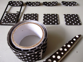 Modern dolls' house miniature black folding chairs with black and white spotty seats and backs, plus a roll of fabric tape and a pair of scissors in the foreground.