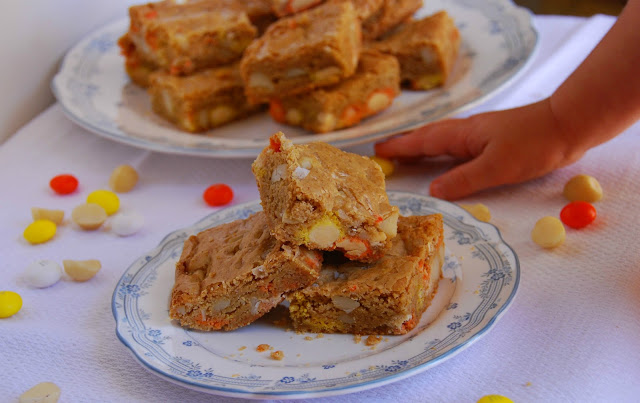 candy corn M&M, roasted macadamia nut, and sea salt blondies on a small plate, with a child's hand reaching for a treat