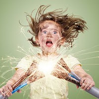 little girl holding electrical cable in both hands with her hair standing on ends and shocked look on her face