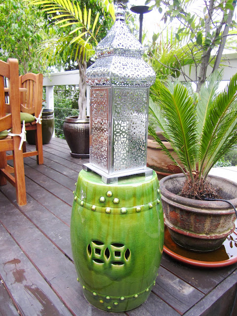 Green ceramic garden stool and a silver lantern on an outdoor deck