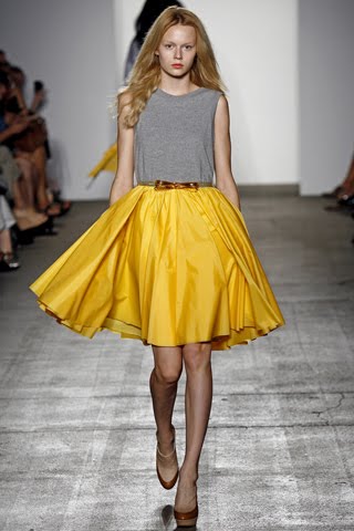 model from Karen Walker's Spring 2011 Ready-to-Wear fashion show wearing a grey short sleeve top with a swing yellow skirt