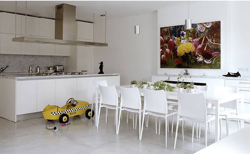 Modern white kitchen with long table, stainless appliances, two silver pendent lights and a child's taxi