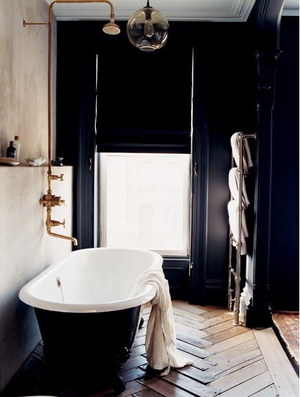 Bathroom with navy walls and a matching stand alone tub, herringbone wood floor, and a door with roman shades for privacy