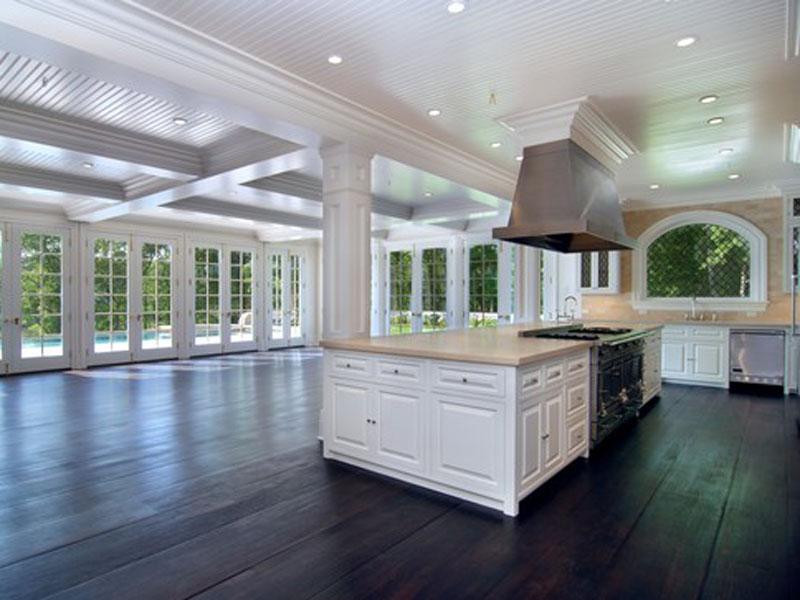 Open kitchen with columns, beadboard ceiling, dark wood floor, marble counter tops and back splash and wrap around French doors and windows