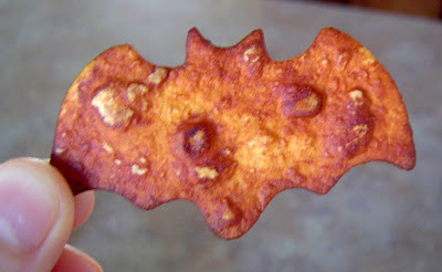 hand holding a bat shaped homemade tortilla chip after baking them to show the deep color