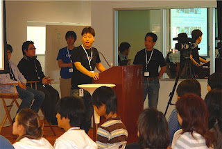 Japan Open House でスピーチをしている方と聞いている方の様子を示す画像。