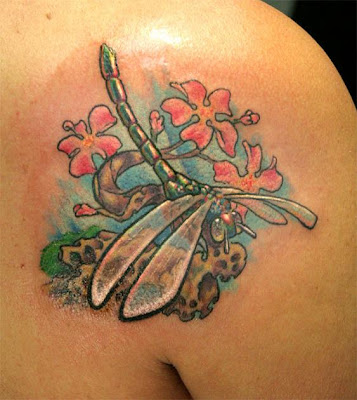 Colorful japanese dragonfly tattoo on the rocks with flowers.
