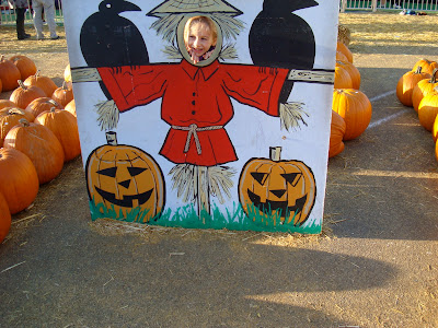 Young girl standing behind painting with face cut out of scarecrow