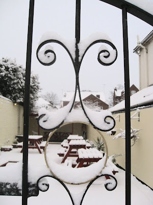 View of the snowy pub garden through a detail in the gates