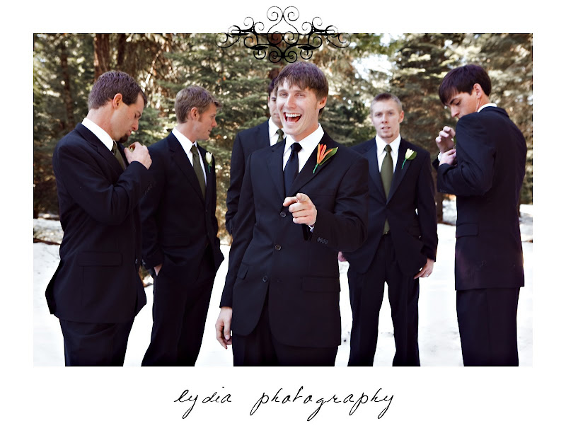 Groom laughing with groomsmen in background at snowy, green and orange wedding in Shingletown, California
