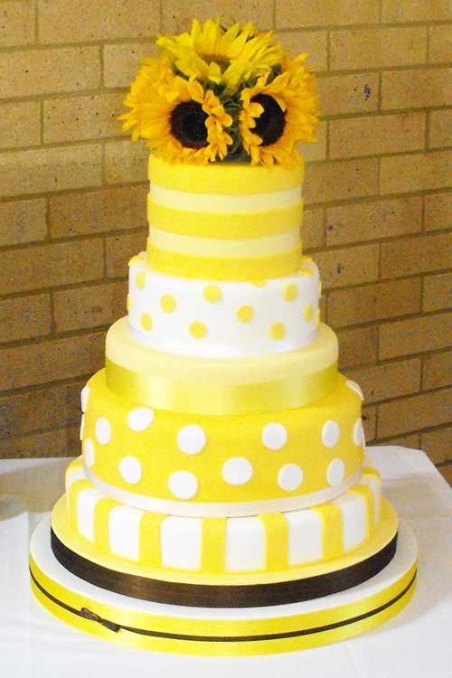 Three tier yellow wedding cake with yellow ribbon and sunflower cake topper