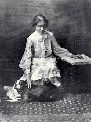 A picture of Helen Keller reading Braille with her left hand and petting her dog with the other hand